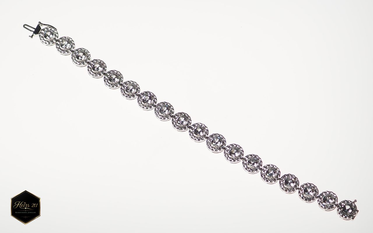 A tennis bracelet of round stones each ringed by a halo of smaller stones, laid out straight