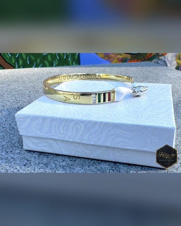 The Curved Paintbrush Bracelet resting on a white gift box outdoors, engraved ABRACADABRA