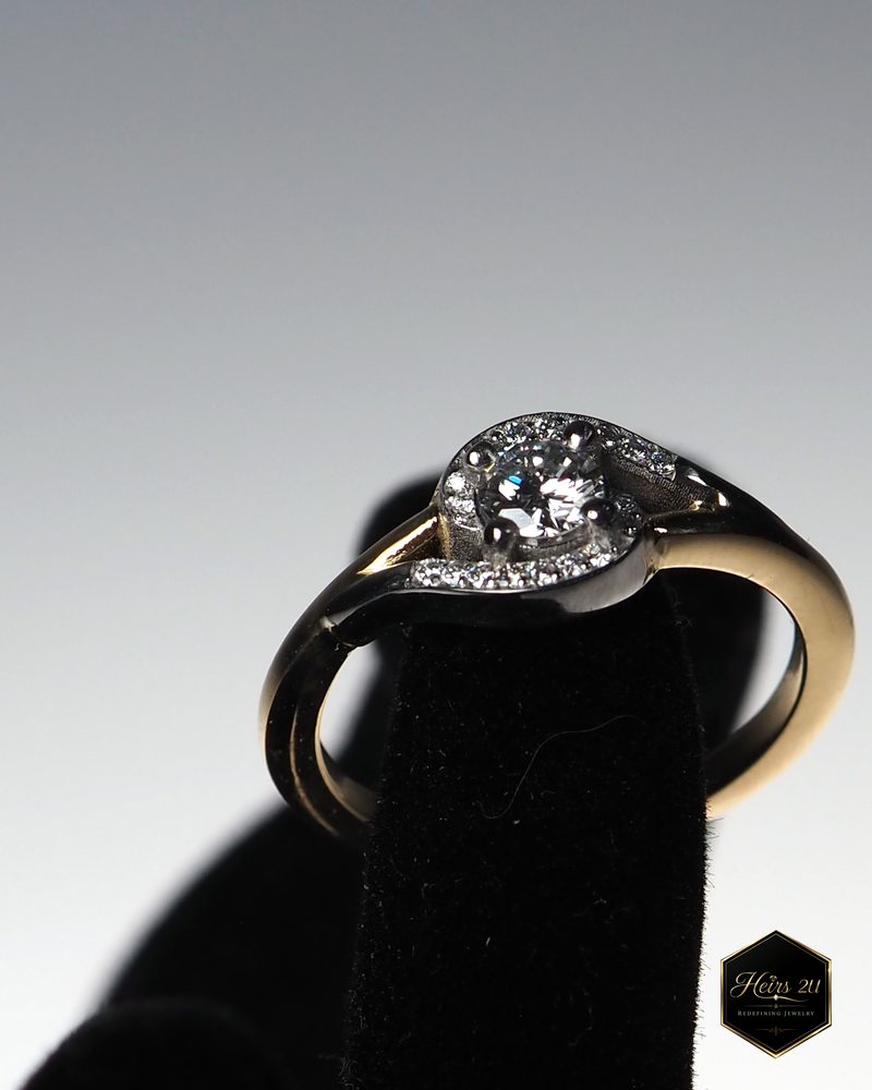 A two-tone bypass ring with a round diamond centre, standing on a black velvet ring display