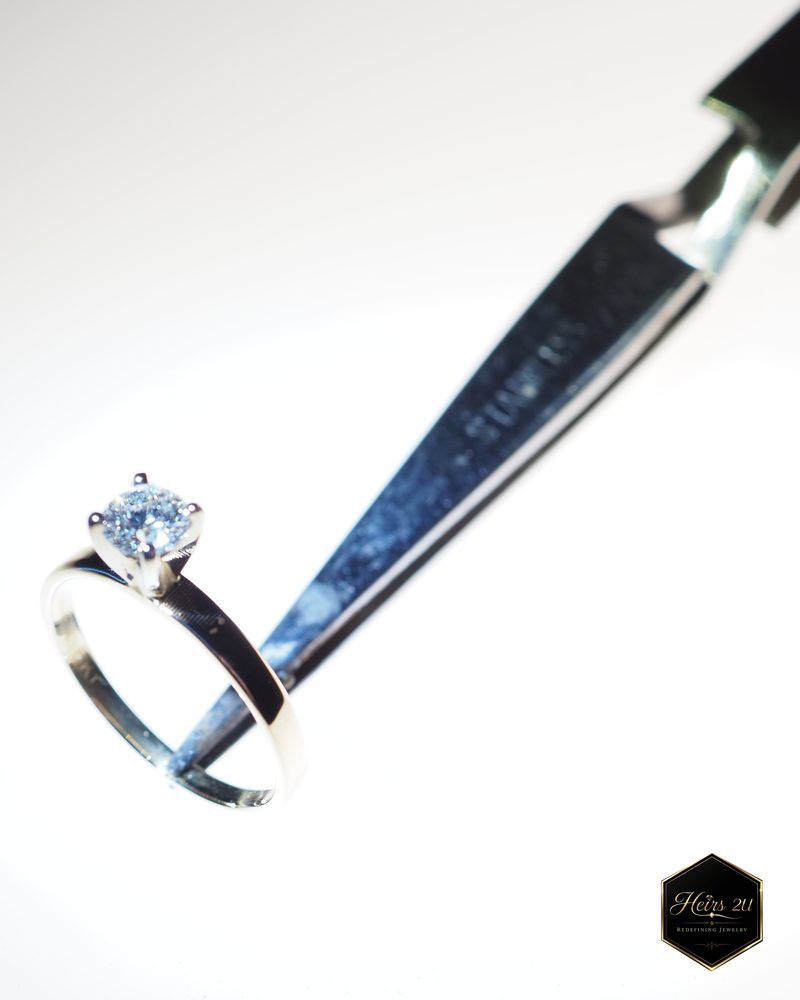 A solitaire ring held in tweezers on the bench while its round centre stone is set