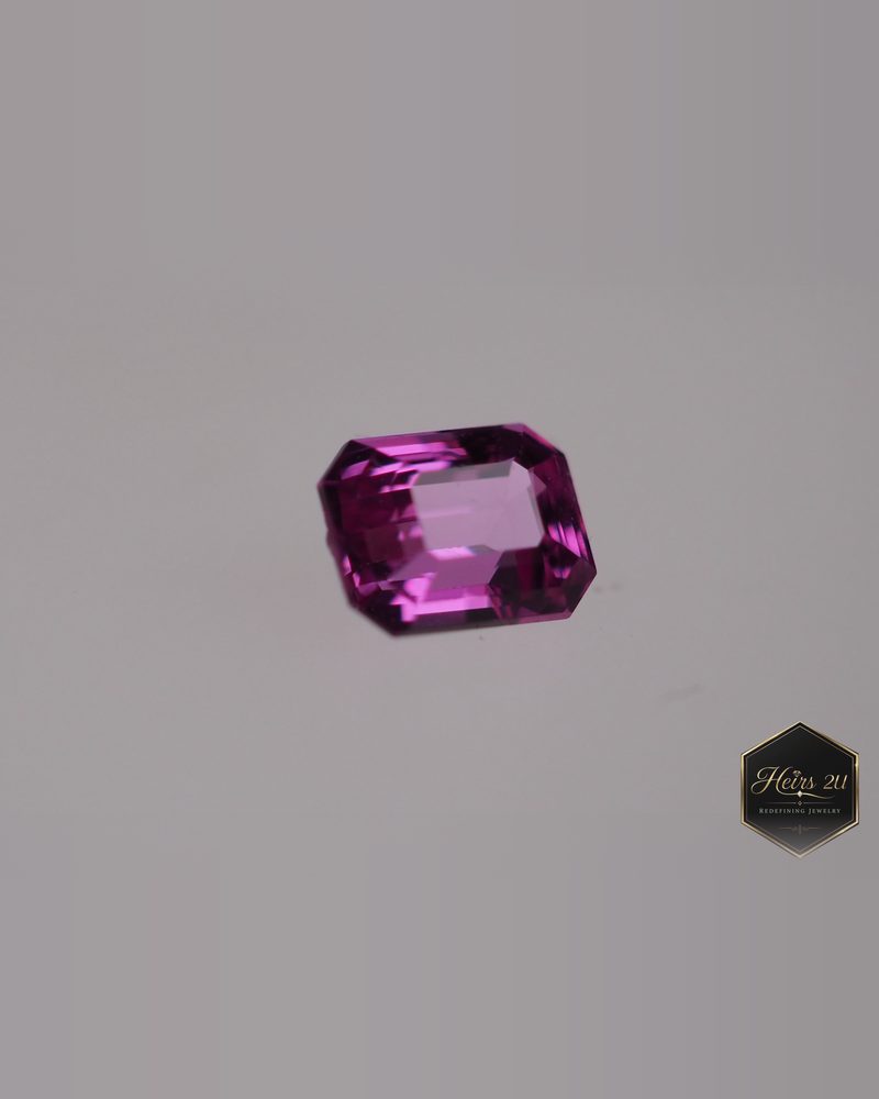 An emerald-cut pink sapphire photographed on grey